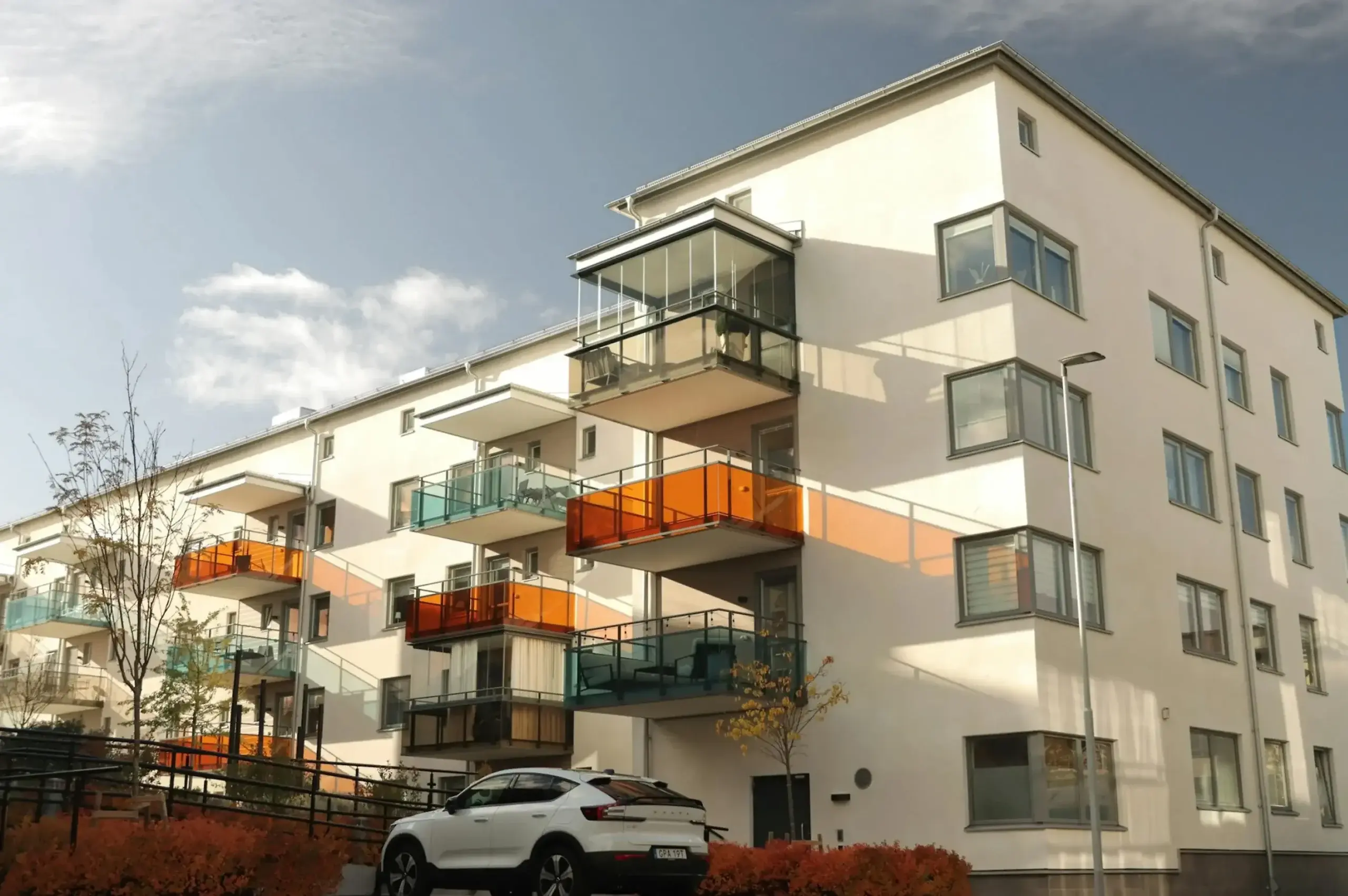 Mehrfamilienhaus mit Balkonen in verschiedenen Farben und geparktem Auto davor